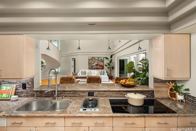 kitchen featuring black electric cooktop, decorative backsplash, light stone countertops, and sink