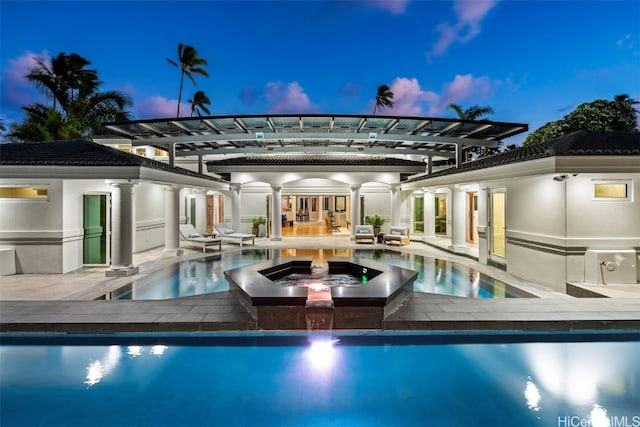 pool at dusk with an in ground hot tub, exterior kitchen, a patio, and a pergola