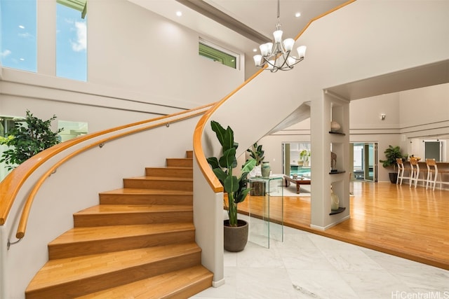 stairs featuring wood-type flooring, a high ceiling, and a chandelier