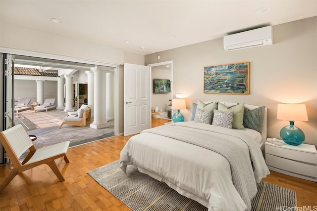 bedroom with decorative columns, wood-type flooring, and a wall unit AC