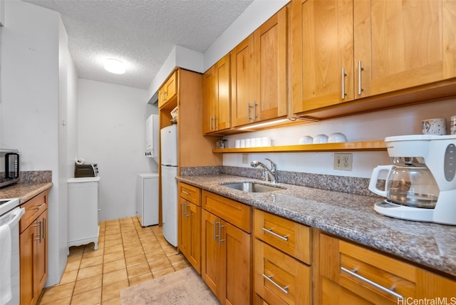 kitchen with light tile patterned floors, sink, white refrigerator, stone counters, and a textured ceiling