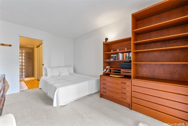 bedroom with a textured ceiling, ensuite bath, and light colored carpet