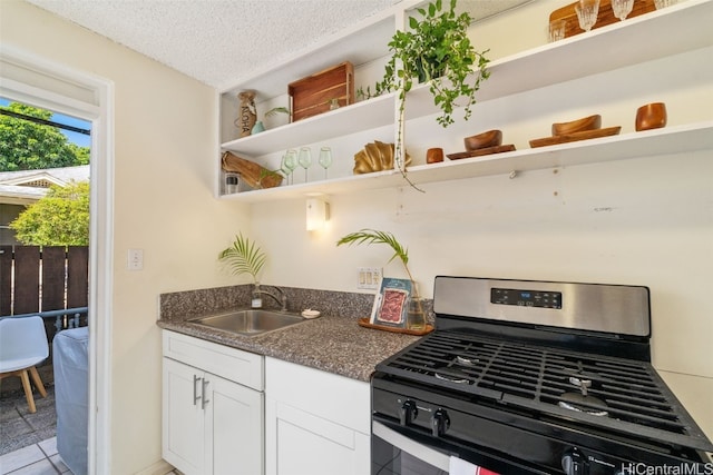 kitchen featuring white cabinetry, sink, stainless steel gas range, tile patterned floors, and a textured ceiling