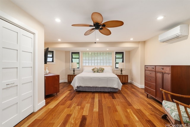 bedroom with a wall unit AC, a closet, light wood-type flooring, and ceiling fan