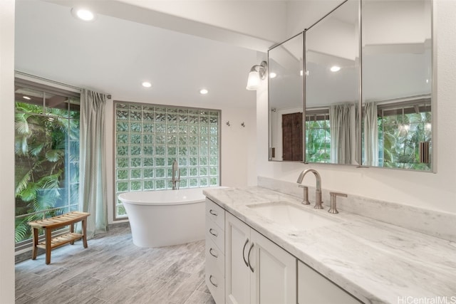 bathroom featuring vanity, a healthy amount of sunlight, hardwood / wood-style flooring, and a bathtub