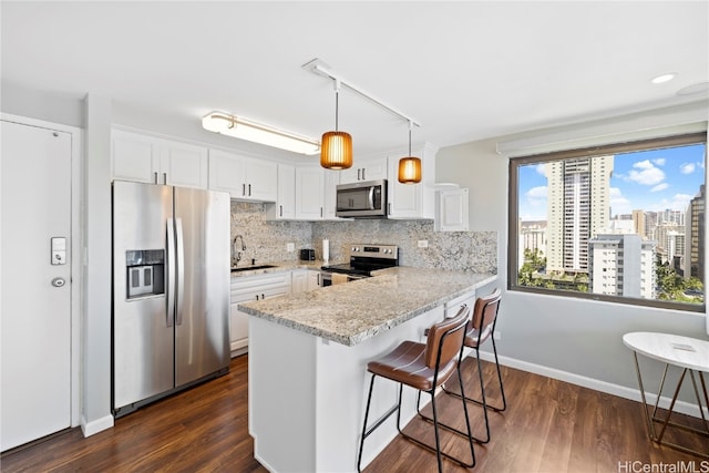 kitchen with appliances with stainless steel finishes, kitchen peninsula, pendant lighting, white cabinets, and light stone counters