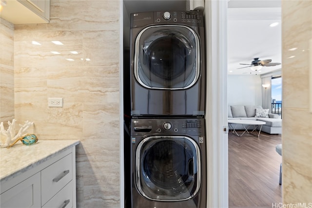 washroom with tile walls, hardwood / wood-style floors, stacked washer and dryer, and ceiling fan