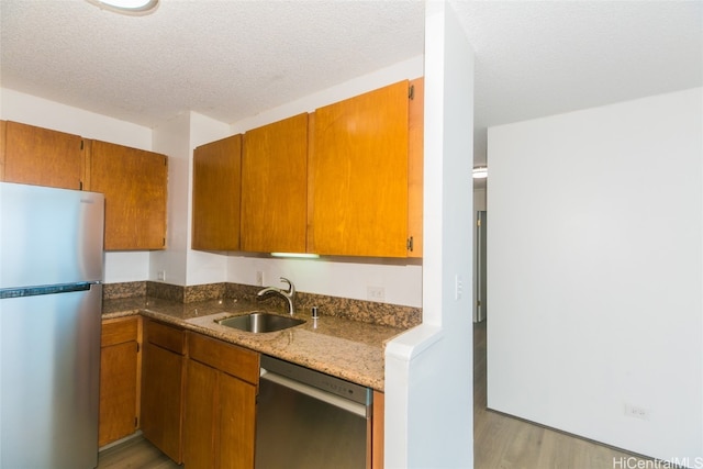 kitchen with sink, a textured ceiling, light hardwood / wood-style floors, stainless steel appliances, and dark stone counters