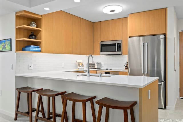 kitchen with decorative backsplash, kitchen peninsula, stainless steel appliances, sink, and a kitchen bar