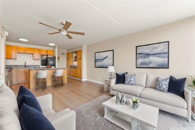 living room featuring ceiling fan, sink, and light wood-type flooring