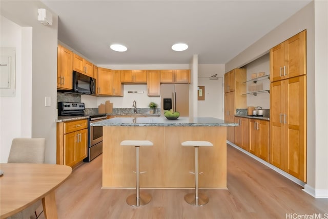 kitchen featuring sink, light wood-type flooring, a center island, a kitchen breakfast bar, and stainless steel appliances