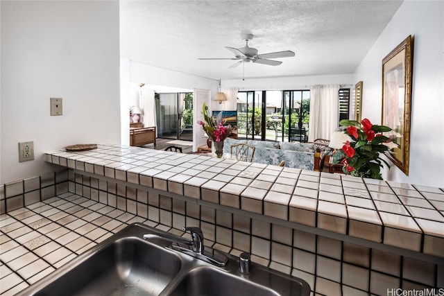 kitchen featuring ceiling fan, a textured ceiling, sink, and tile counters