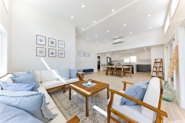 living room with an AC wall unit, a high ceiling, light hardwood / wood-style flooring, and sink