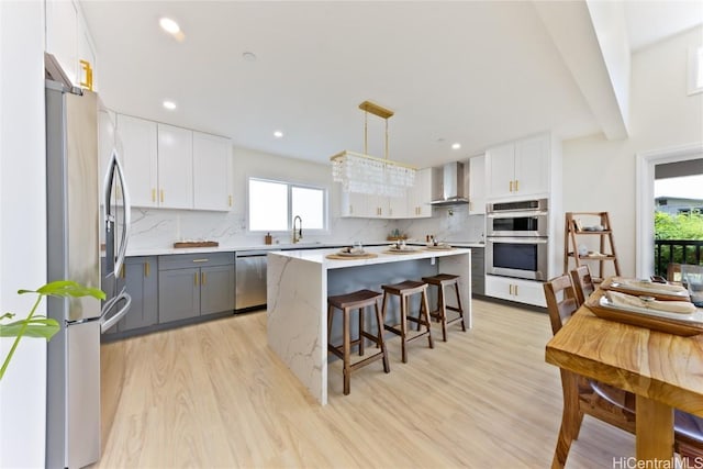 kitchen with decorative light fixtures, white cabinets, wall chimney range hood, and stainless steel appliances