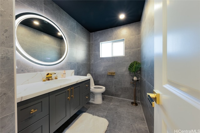 bathroom with toilet, tile patterned flooring, vanity, and tile walls