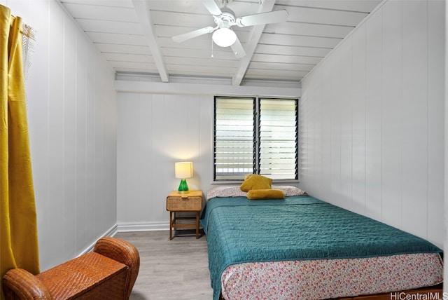 bedroom featuring beamed ceiling, hardwood / wood-style floors, ceiling fan, and wooden walls