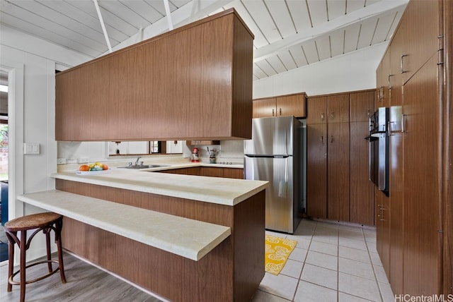 kitchen featuring sink, a kitchen breakfast bar, kitchen peninsula, stainless steel fridge, and light tile patterned floors