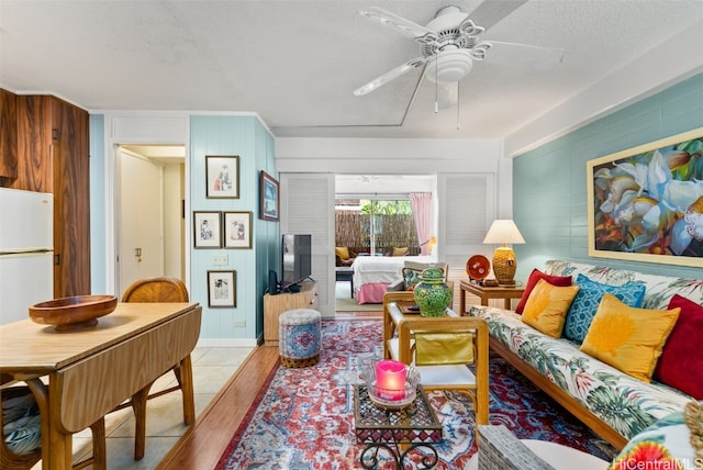 living room featuring light hardwood / wood-style floors, wood walls, a textured ceiling, and ceiling fan