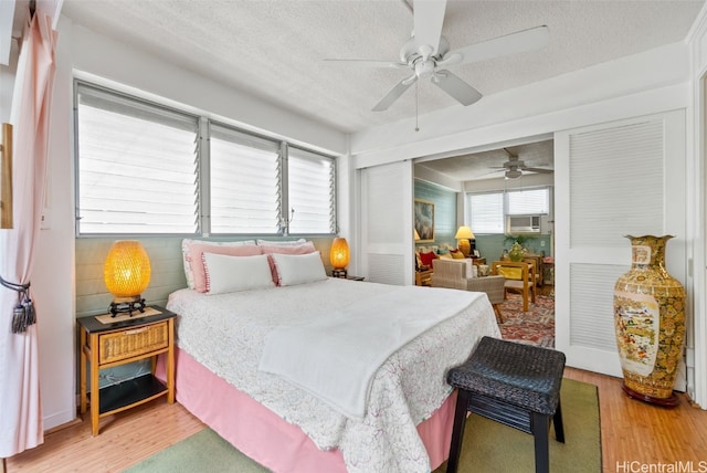 bedroom with a textured ceiling, cooling unit, wood-type flooring, and ceiling fan