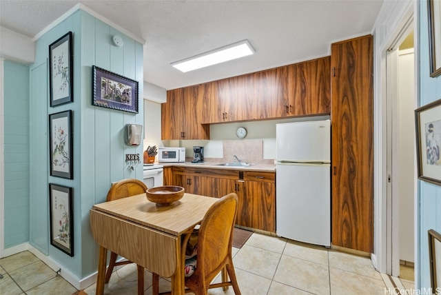 kitchen featuring white appliances, wood walls, sink, light tile patterned flooring, and a textured ceiling