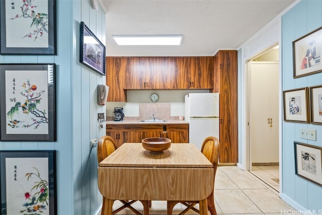 kitchen with wood walls, sink, light tile patterned floors, and white refrigerator