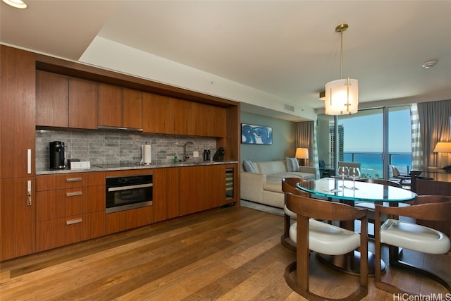 kitchen with backsplash, stainless steel oven, dark hardwood / wood-style flooring, decorative light fixtures, and a water view