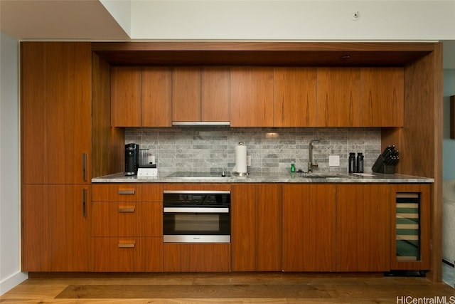 kitchen featuring decorative backsplash, hardwood / wood-style flooring, black electric cooktop, oven, and sink