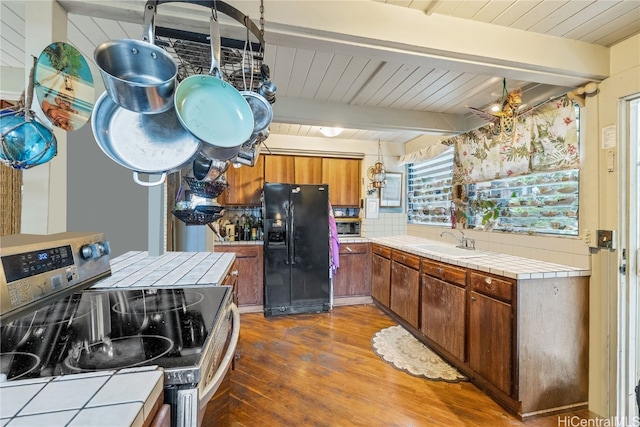 kitchen with black refrigerator with ice dispenser, tile counters, stainless steel range with electric cooktop, and dark hardwood / wood-style flooring