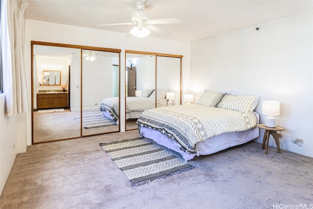 bedroom featuring a textured ceiling, carpet, two closets, and a ceiling fan