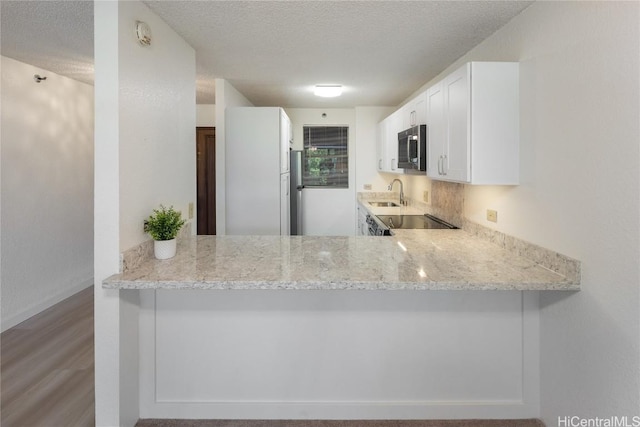 kitchen featuring a textured ceiling, light stone counters, a sink, white cabinetry, and stainless steel microwave