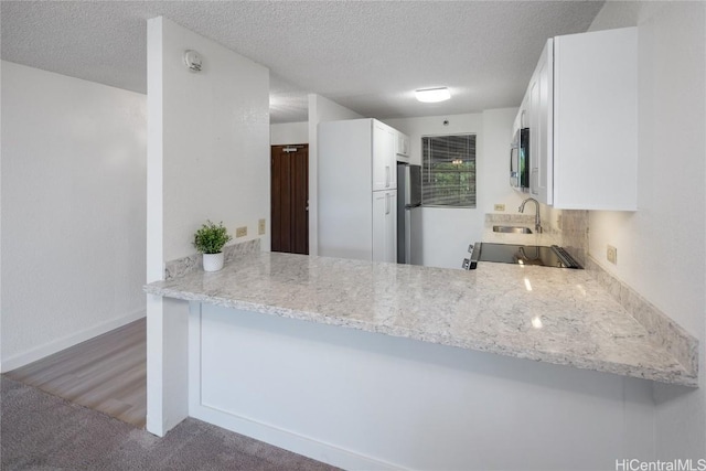 kitchen with a textured ceiling, stainless steel appliances, a peninsula, a sink, and white cabinetry