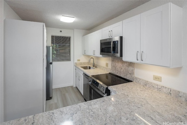 kitchen featuring appliances with stainless steel finishes, white cabinetry, a sink, a textured ceiling, and light stone countertops