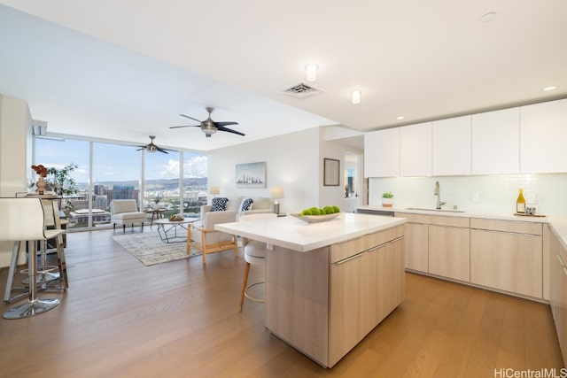 kitchen with tasteful backsplash, sink, light wood-type flooring, a kitchen island, and a kitchen breakfast bar