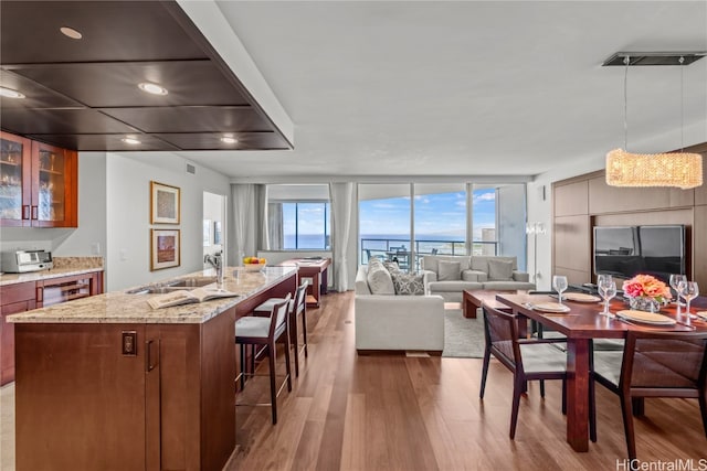 kitchen with hardwood / wood-style flooring, an island with sink, hanging light fixtures, sink, and a breakfast bar