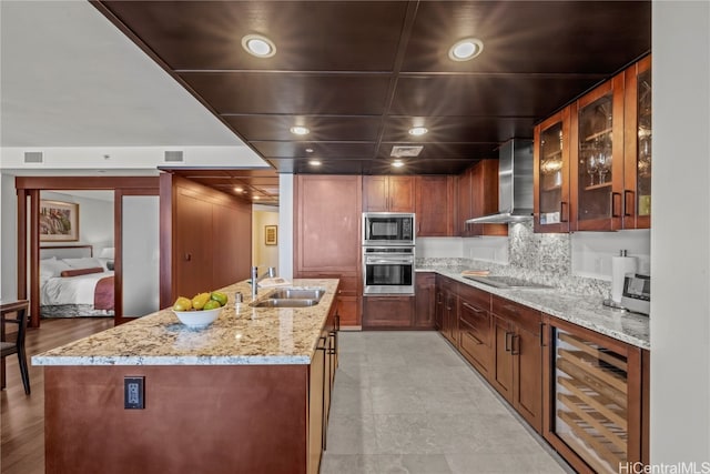 kitchen with wall chimney range hood, sink, an island with sink, stainless steel appliances, and wine cooler