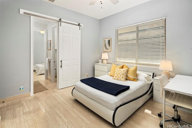 bedroom with ceiling fan, a barn door, and light hardwood / wood-style floors