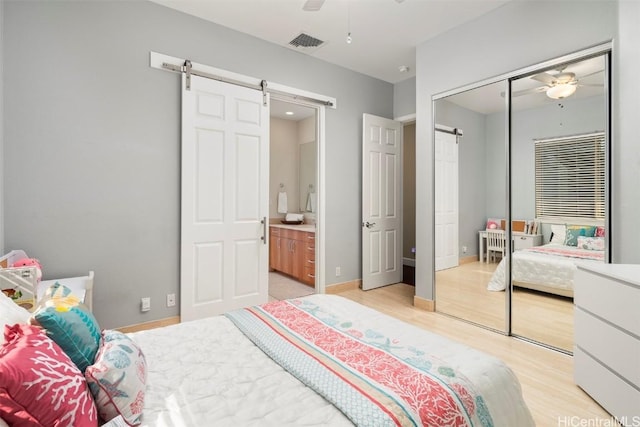 bedroom featuring light wood-type flooring, ceiling fan, a barn door, connected bathroom, and a closet