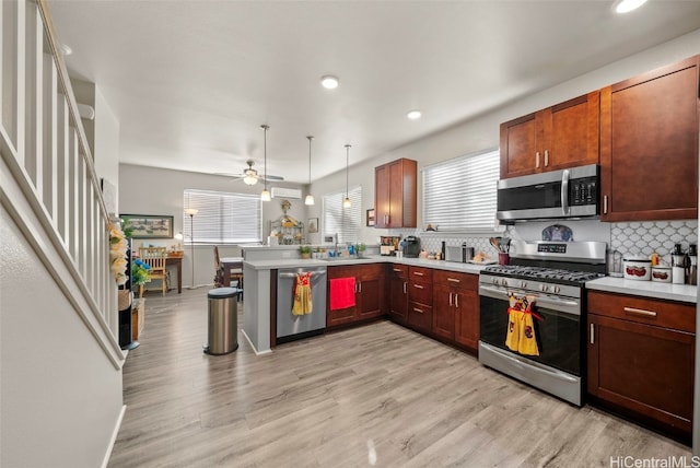 kitchen featuring appliances with stainless steel finishes, kitchen peninsula, light hardwood / wood-style flooring, and pendant lighting