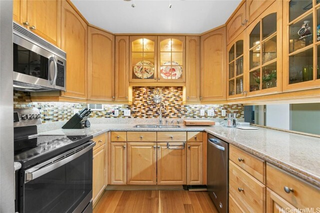 kitchen with backsplash, sink, light stone countertops, light hardwood / wood-style floors, and stainless steel appliances