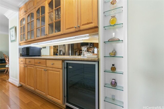 bar with light wood-type flooring, beverage cooler, and crown molding