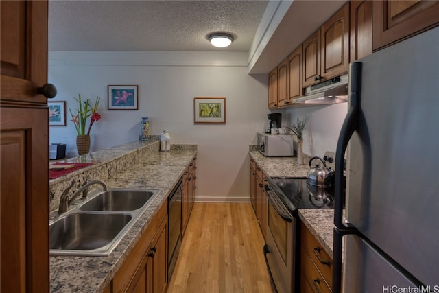 kitchen with a textured ceiling, light stone countertops, light hardwood / wood-style flooring, sink, and stainless steel appliances