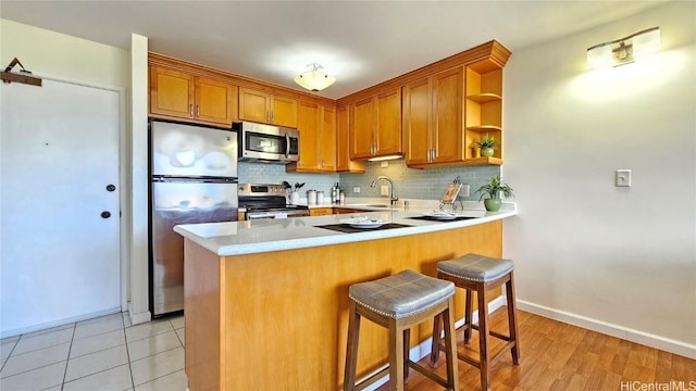 kitchen with appliances with stainless steel finishes, a breakfast bar, tasteful backsplash, sink, and kitchen peninsula