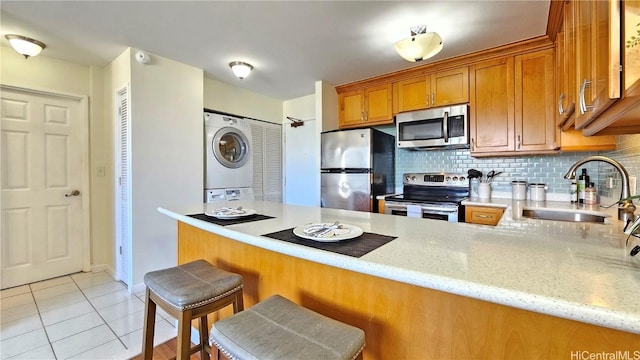 kitchen featuring backsplash, stainless steel appliances, stacked washer / dryer, light tile patterned flooring, and kitchen peninsula