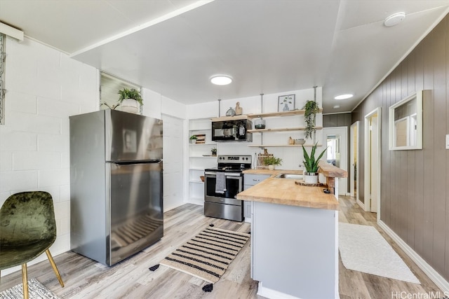 kitchen featuring appliances with stainless steel finishes, wood walls, butcher block counters, and light wood-type flooring