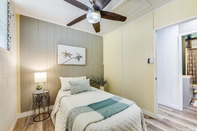 bedroom featuring ceiling fan, crown molding, light wood-type flooring, and wood walls