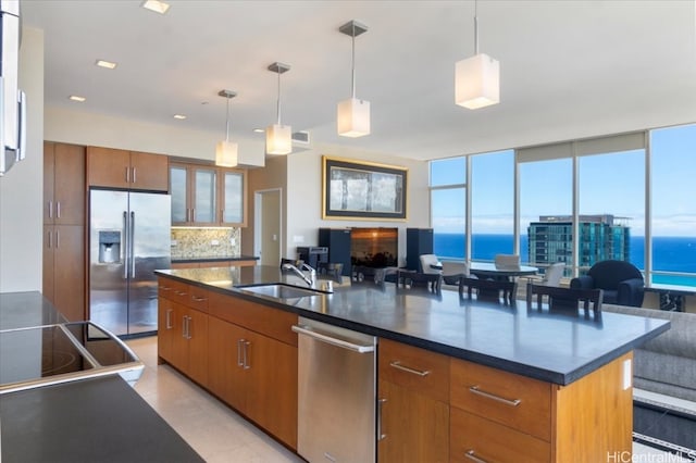 kitchen with tasteful backsplash, hanging light fixtures, a kitchen island with sink, sink, and stainless steel appliances