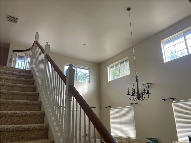 staircase featuring visible vents, a towering ceiling, and a notable chandelier