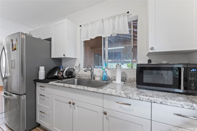 kitchen with white cabinetry, stainless steel appliances, sink, and light stone counters