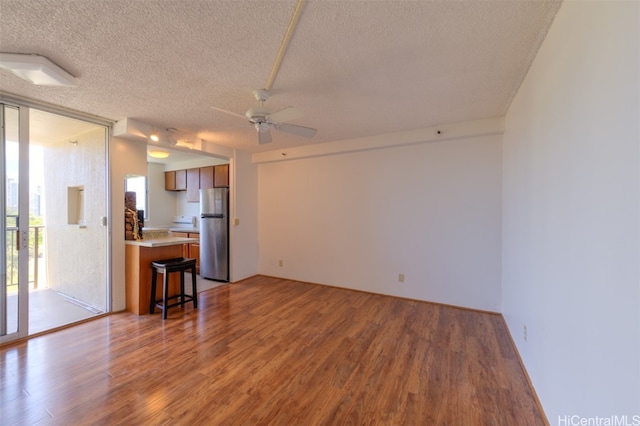 unfurnished living room featuring expansive windows, a textured ceiling, light wood-type flooring, and ceiling fan