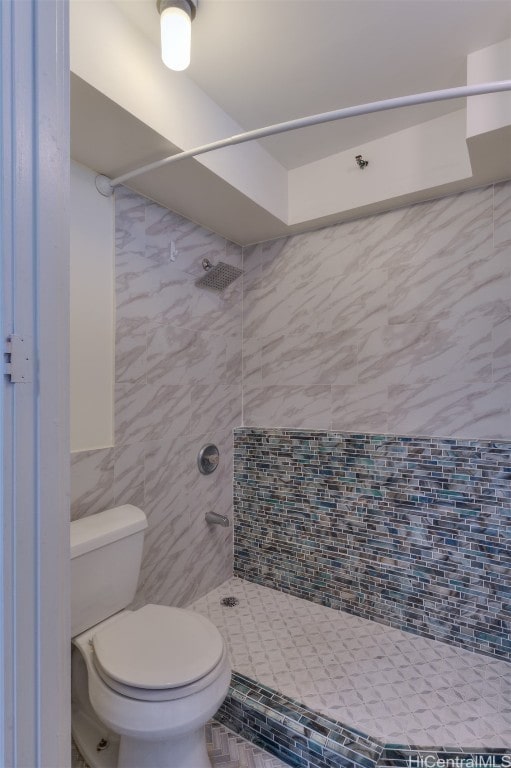 bathroom with tile walls, a tile shower, and toilet